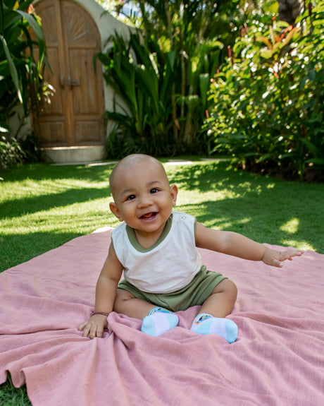 Baby sitting in garden on blanket wearing babywear manufactred by CM Garmindo.